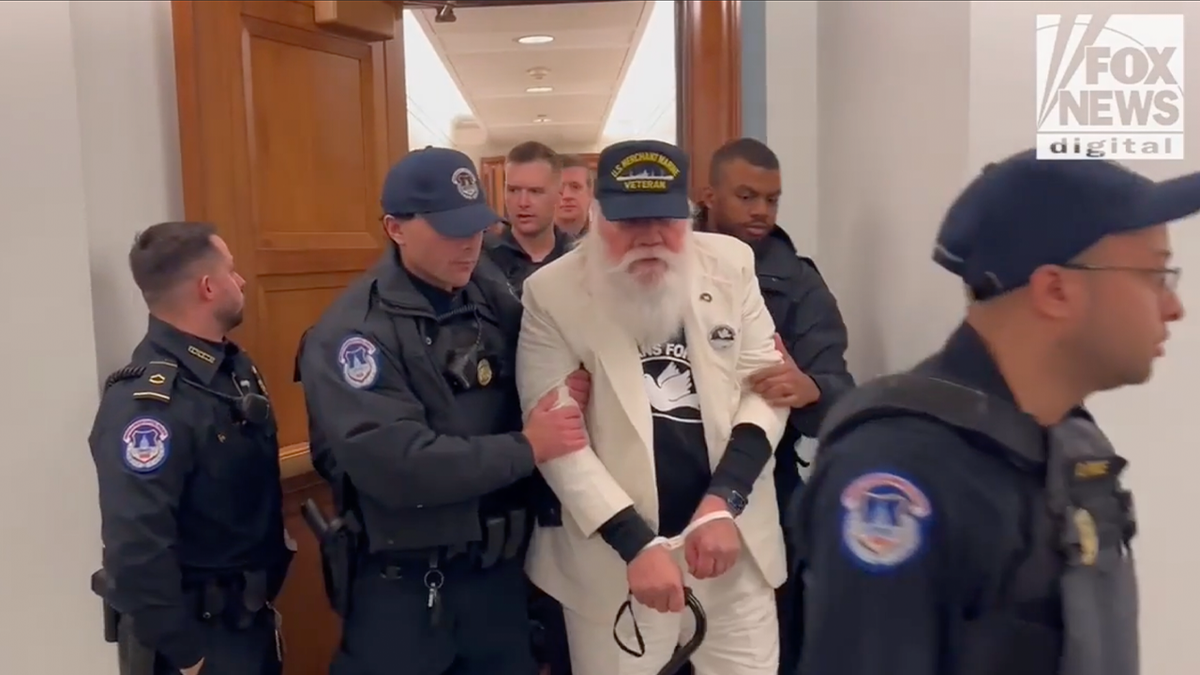 white haired male protester escorted by police