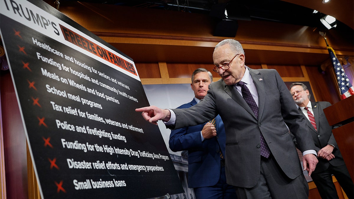 Sen. Chuck Schumer points to a chart laying out programs at risk from President Donald Trump's pause on federal assistance