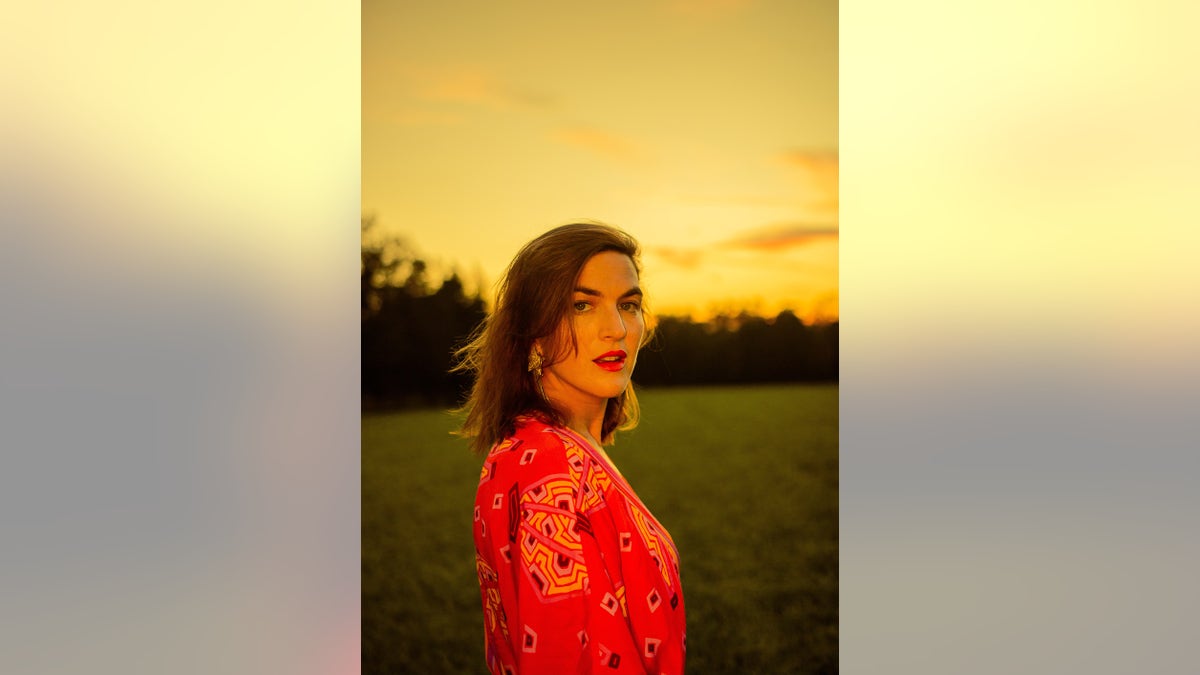 Laura Warshauer wearing a floral coral dress in a field during sunset.