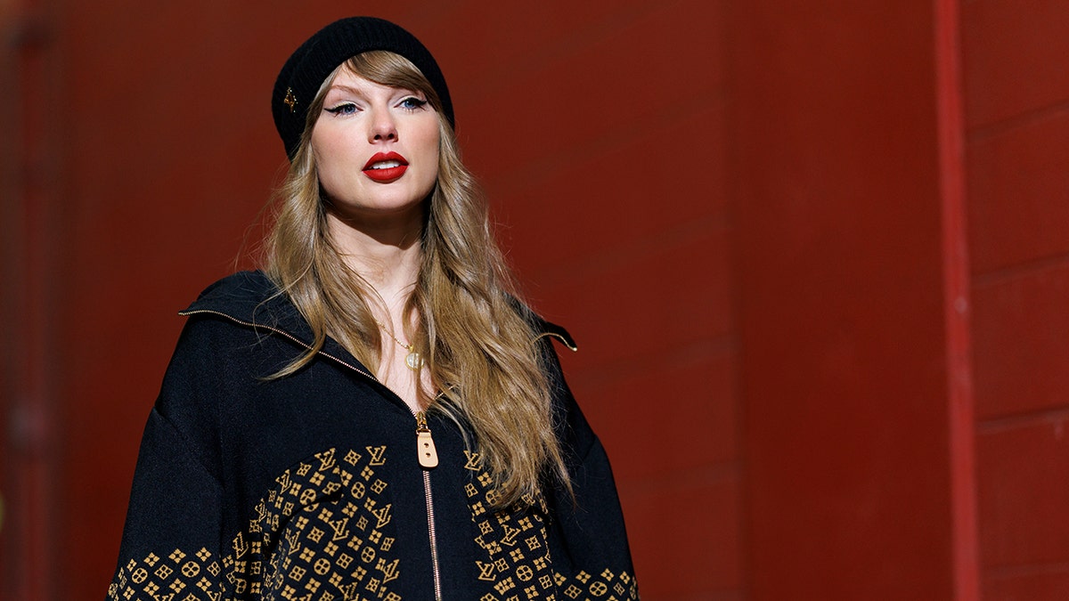 Taylor Swift walks down a hallway wearing a Louis Vuitton jacket and hat 