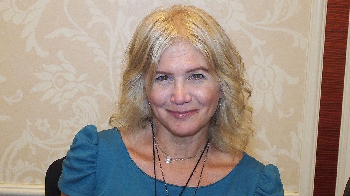 Tracey Gold in a blue top with poofy ruffled shoulder soft smiles for a photo