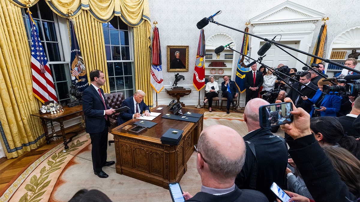 President Trump signs executive orders while taking questions from the press. 