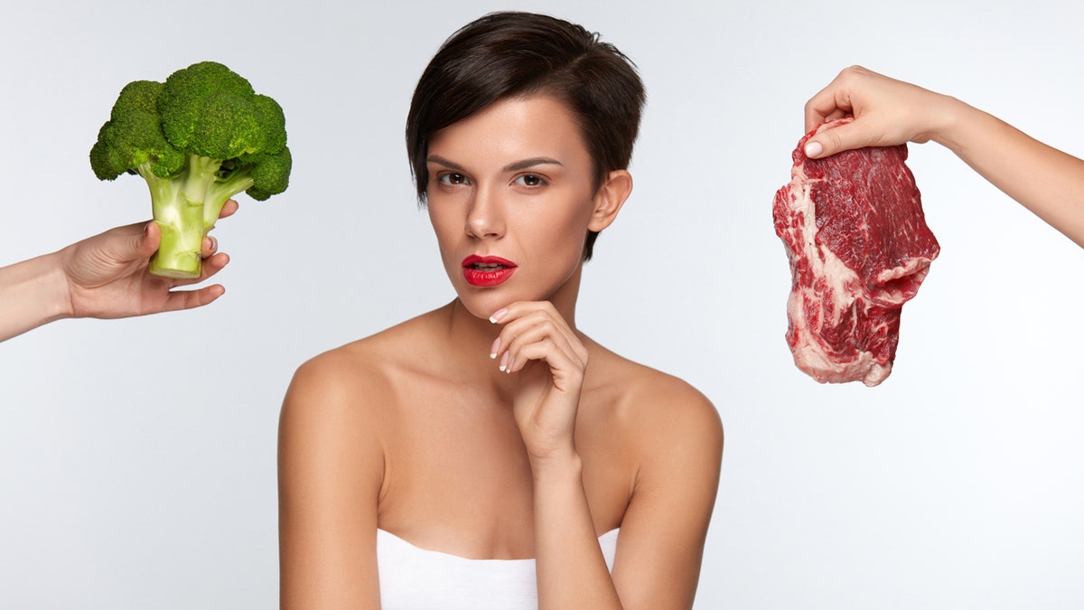 A healthy eating, beautiful woman with red lips is choosing between raw steak and broccoli, thinking whether to eat vegetables or meat.