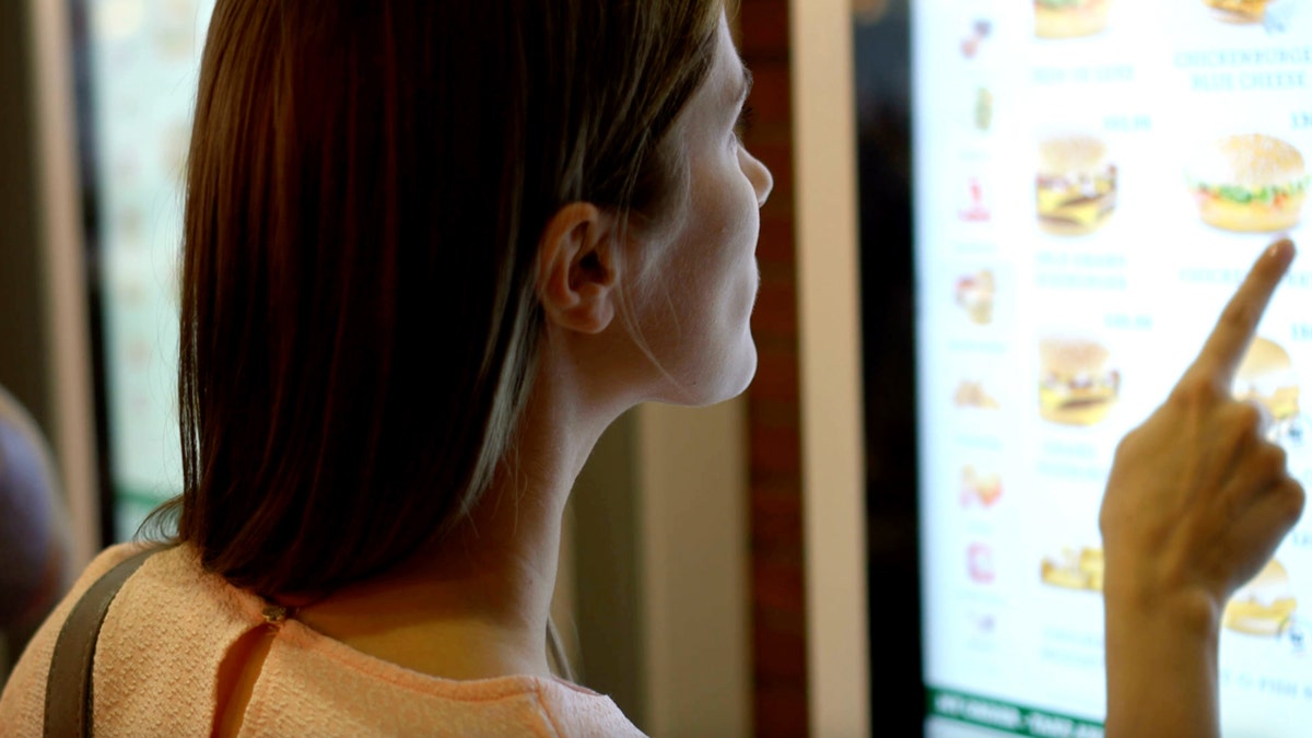 A woman orders fast food from a digital self-serve screen.