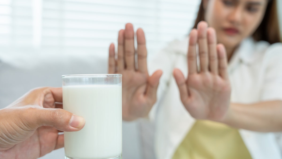 A woman holds out her hands to reject a glass of milk being offered to her.