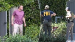 Ben Affleck in a maroon shirt and tan slacks looks angsty as he stands outside his home in Brentwood split a man in a navy blue FBI jacket stands with his back to the camera next to another gentleman in a green FBI jacket outside Ben Affleck's home