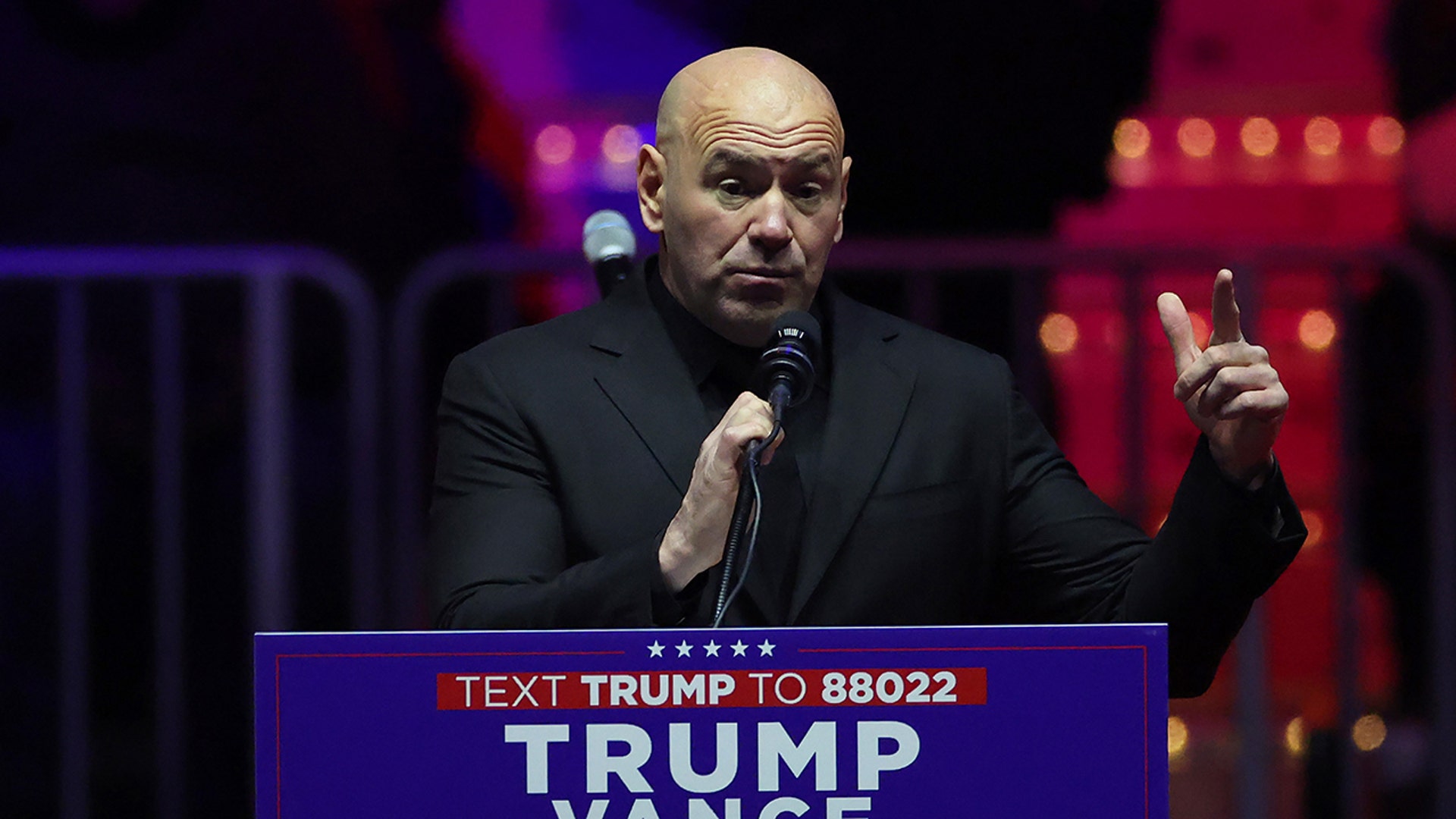 UFC Ceo Dana White in a black suit speaks behind the podium at Trump's MAGA Victory Rally