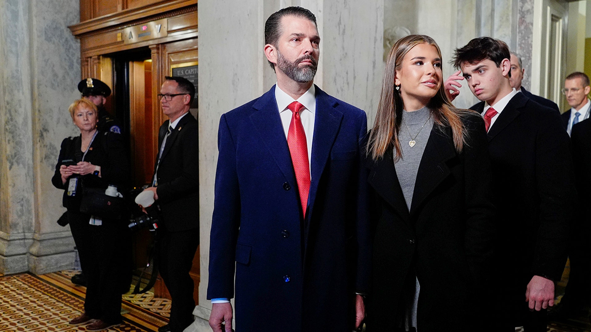 Donald Trump Jr. in a blue suit and red tie walks into the Rotunda with his daughter Kai Trump in a black jacket