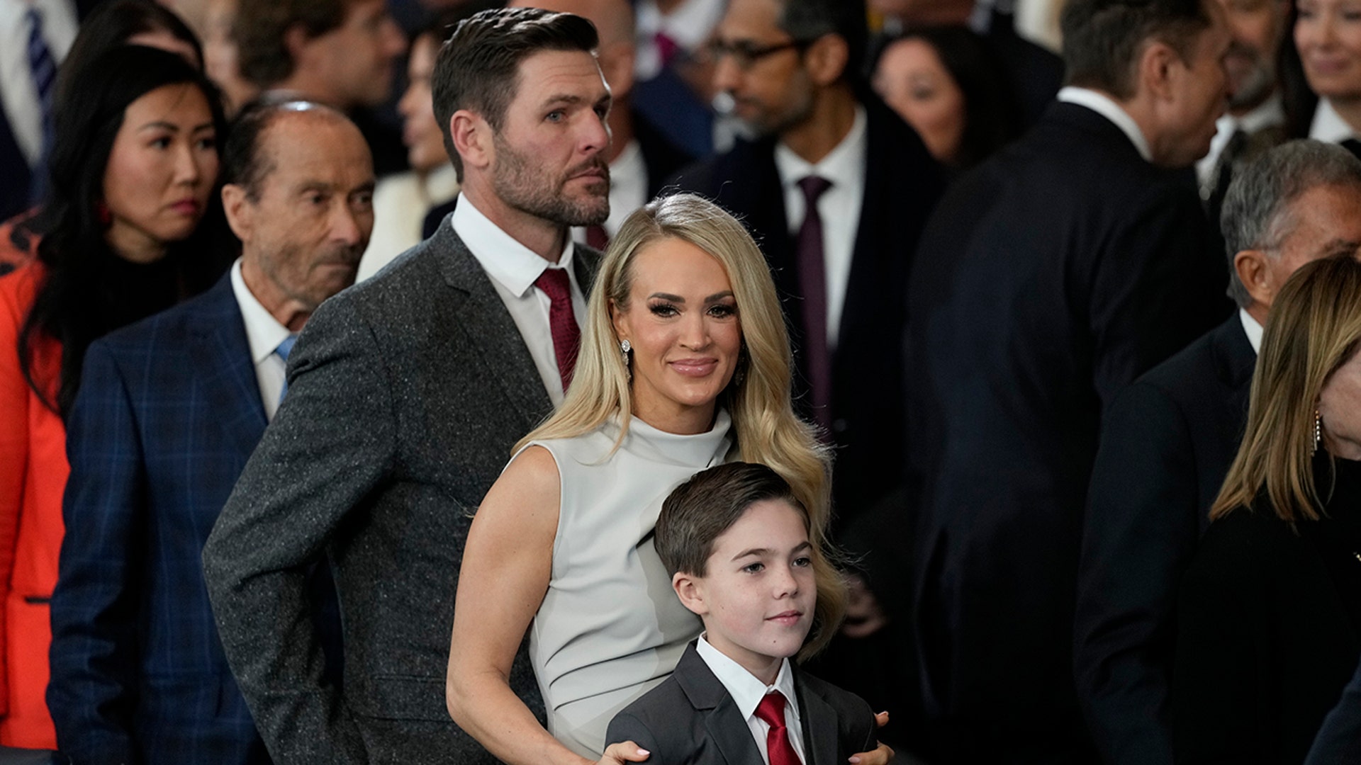 Mike Fisher stands behind his wife Carrie Underwood in a gray dress who holds onto her son Isaiah
