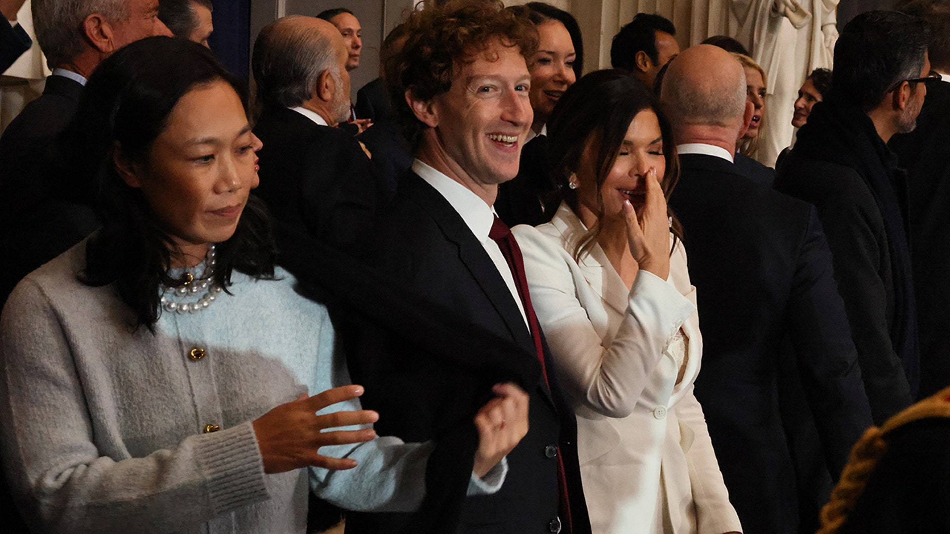 Mark Zuckerberg laughs alongside Lauren Sánchez, wearing a cream jacket covering her mouth
