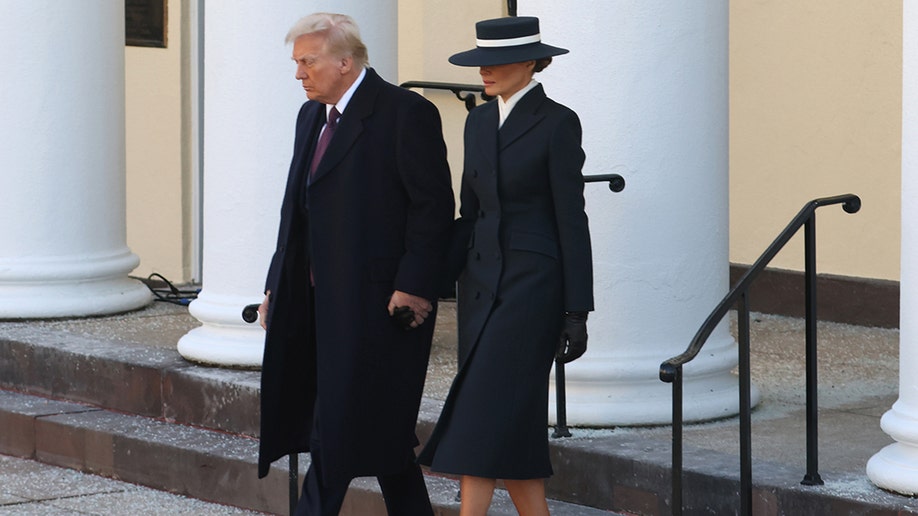 Donald Trump in a black overcoat walks hand in hand with wife Melania in a black overcoat and matching black hat with a white stripe