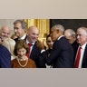 Dana White in a dark suit and red tie converses with former President Obama as his wife stands beside him and former First Lady Laura Bush walks out of frame