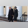 Donald Trump in a black overcoat walks hand in hand with wife Melania in a black overcoat and matching black hat with a white stripe