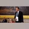 Elon Musk in a dark suit with a paper to his chest stands in the Rotunda