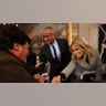 Robert F. Kennedy Jr. in a black suit and tie and wife and actress Cheryl Hines in a houndtooth jacket lean over and shake the hands of people as they leave the inauguration