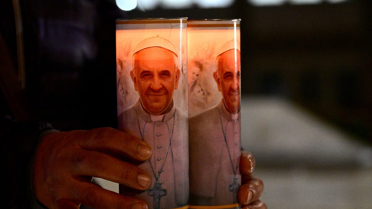 A faithful from Bolivia holds candles of Pope Francis near a statue of Pope John Paul II outside the Gemelli hospital where Pope Francis is hospitalized for tests and treatment for bronchitis in Rome, on February 18, 2025.