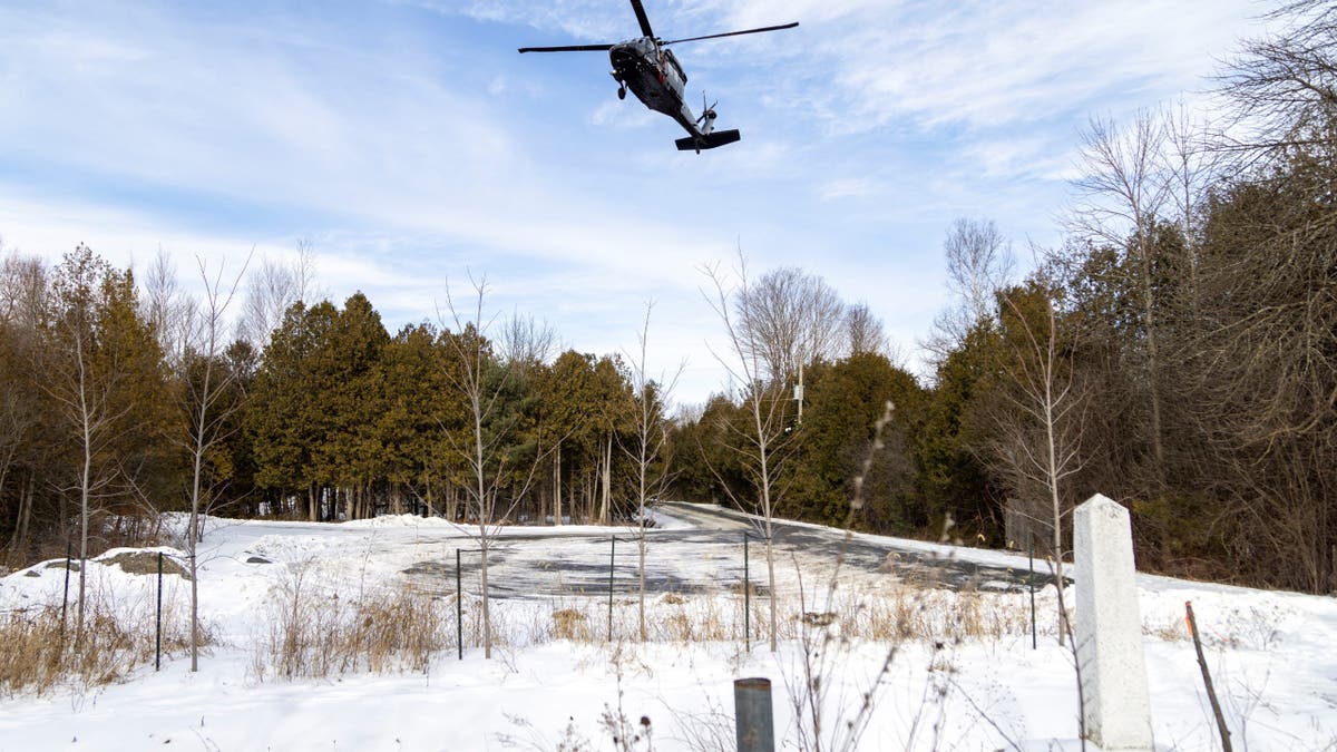A Royal Canadian Mounted Police Blackhawk helicopter flies above US-Canada border marker with snow on the ground