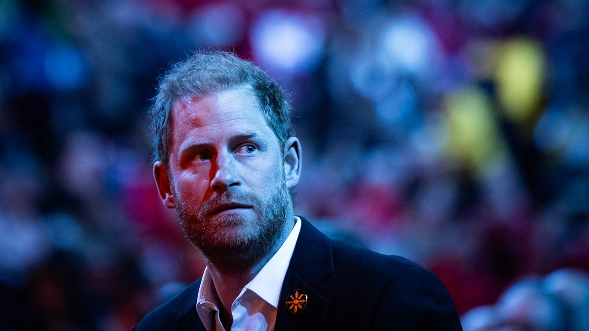 Prince Harry looking serious in a crowd wearing a suit