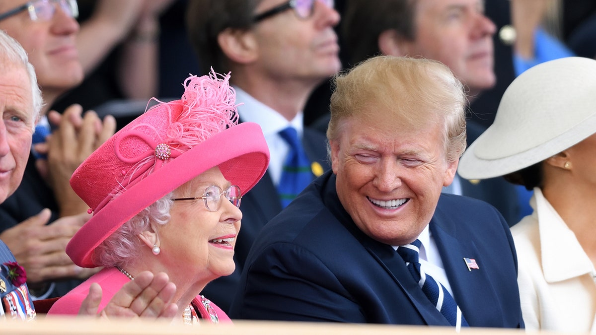 President Trump smiling and looking at Queen Elizabeth who is wearing a