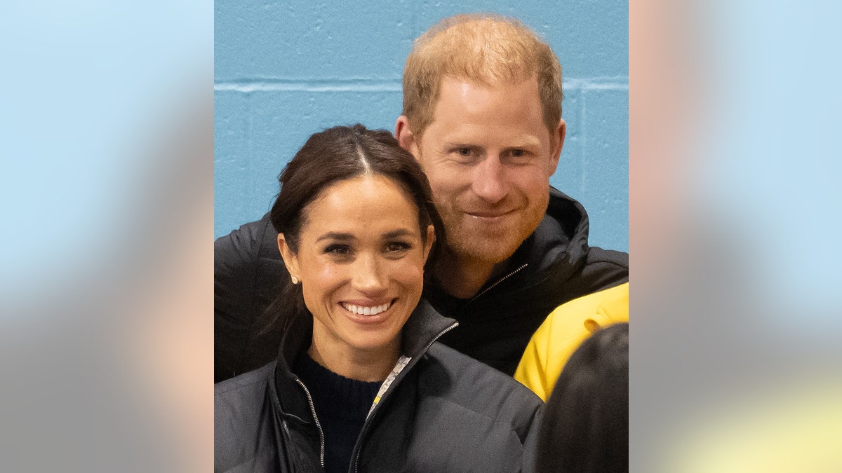 Prince Harry posing behind a smiling Meghan Markle for a photo.