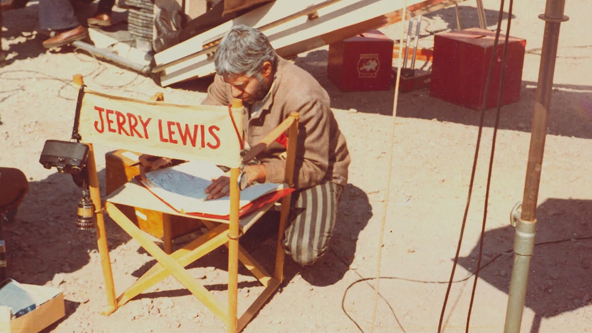 Jerry Lewis kneeling on a chair writing on a script.