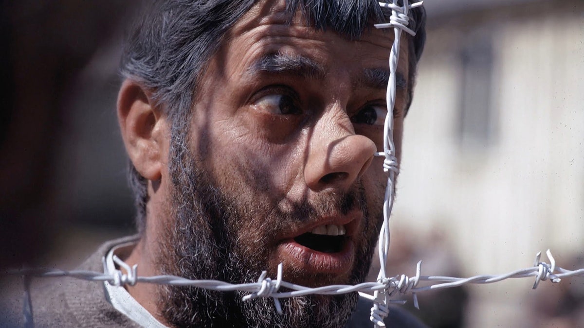 A close-up of Jerry Lewis in costume behind a barb wired fence.