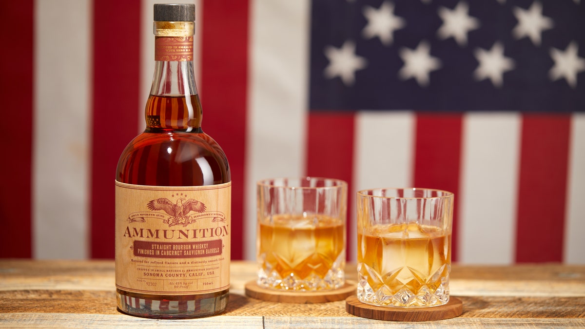 A vessel  of Ammunition whiskey is shown connected  a woody  array  adjacent  to 2  glasses with an American emblem  arsenic  a backdrop.