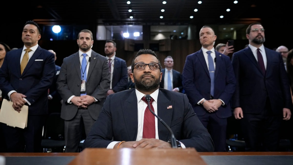 Cash Patel is sitting on the table, while others are behind it