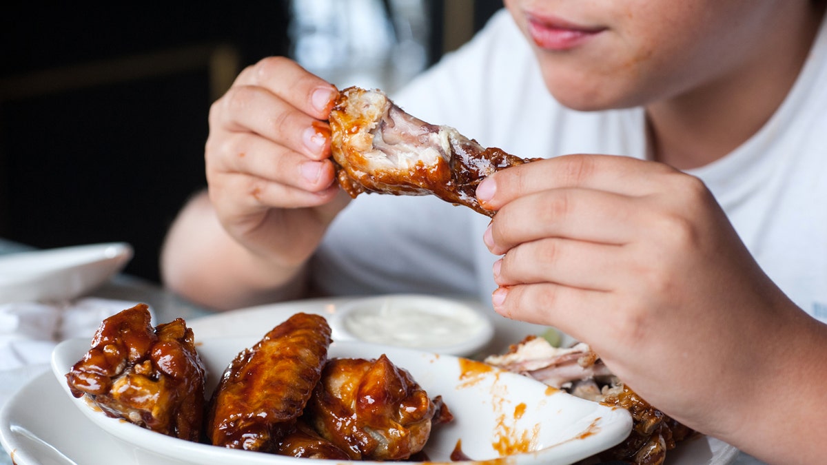 A boy is shown eating a buffalo wing.