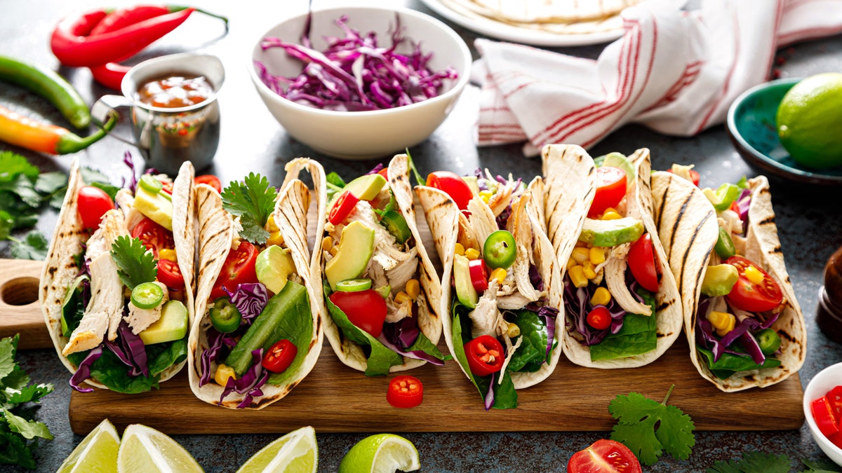 Six chicken tacos are shown on a platter near a bowl of red cabbage.