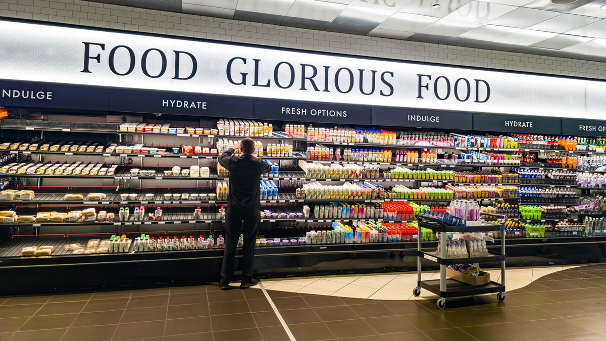 A antheral   stocks drinks successful  the refrigerated conception  of a convenience store   nether  a motion   that reads "Food Glorious Food."