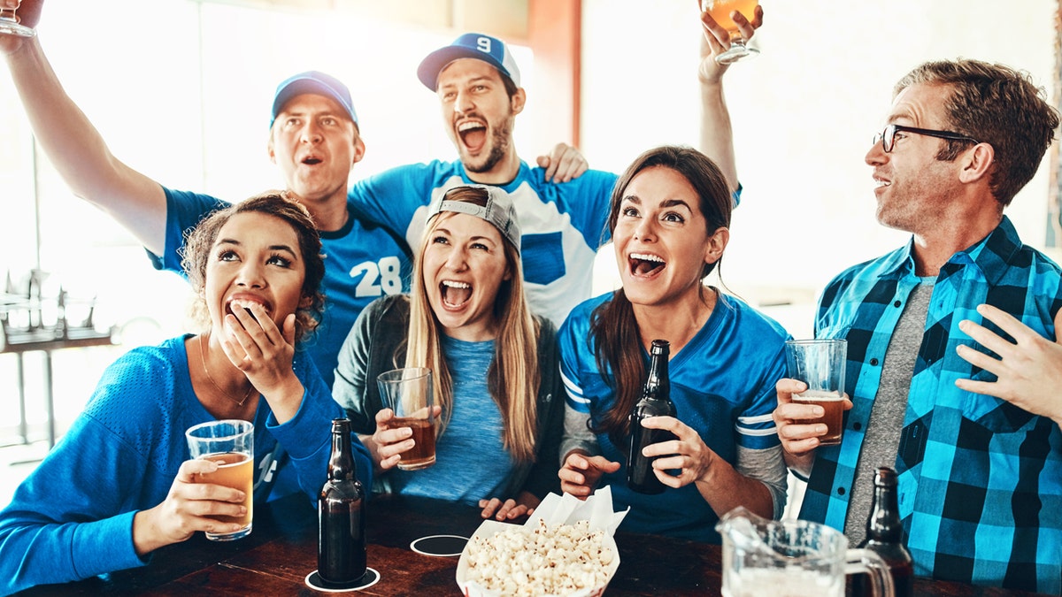 Football fans celebrate while drinking beer with corn popcorn at the table.