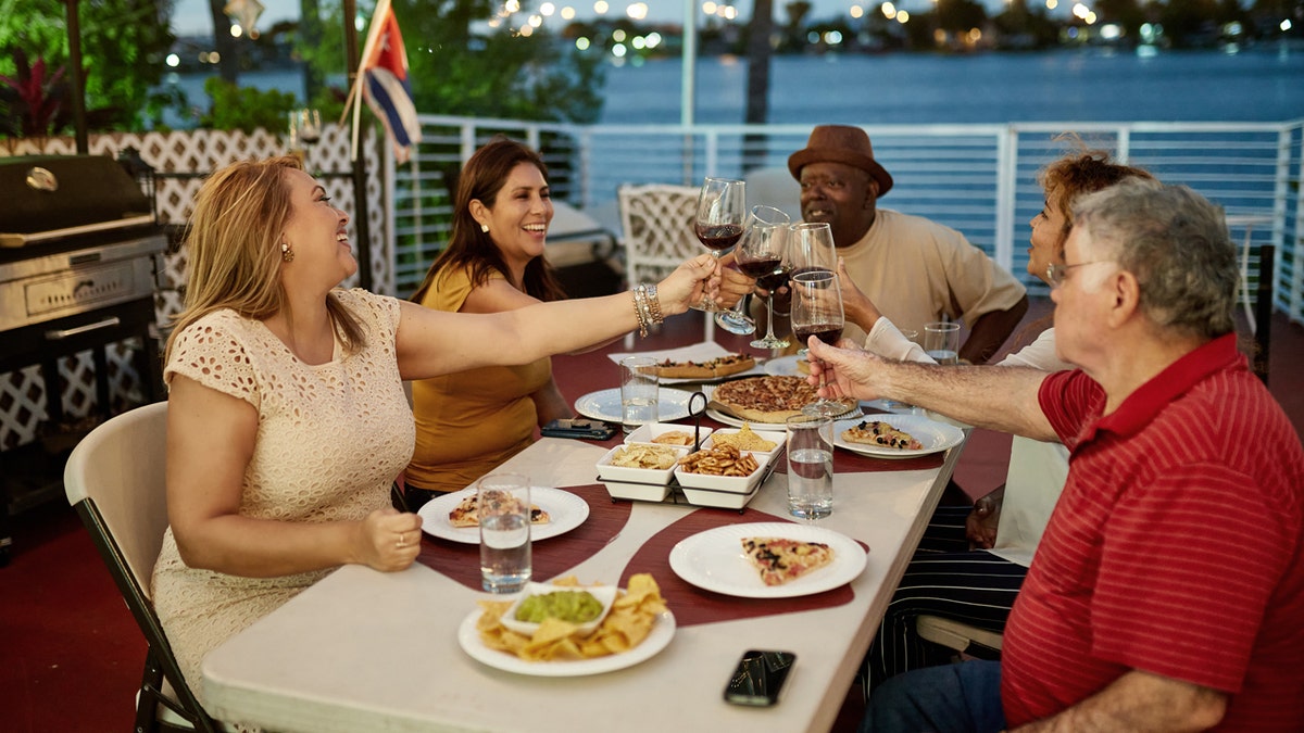 Five friends raise the wine cups and collect them to toast while eating along the waterfront.