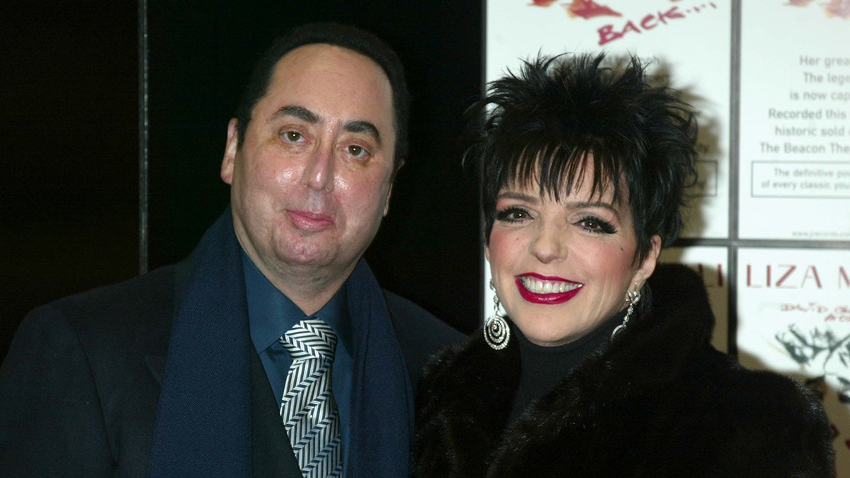 Liza Minnelli wearing black and silver dangling earrings smiling next to David Gest wearing a blue suit and a silver and black tie.
