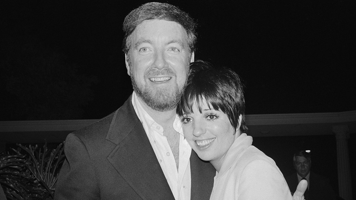 Liza Minnelli wearing white leaning on on a smiling Jack Haley Jr. wearing an open white shirt and a dark blazer.