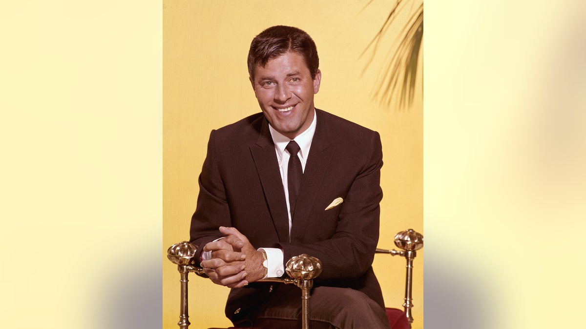 A close-up of Jerry Lewis smiling wearing a brown suit against a yellow background.