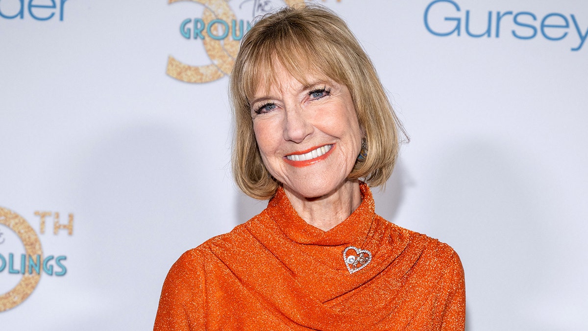 A close-up of Karen Knotts smiling and wearing an orange dress with a brooch