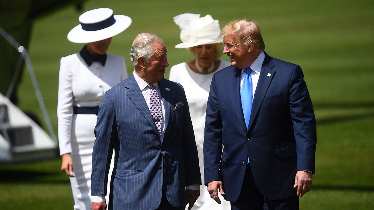 King Charles and President Trump walking next to each other side by side smiling with their wives behind