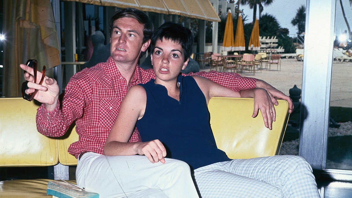 Peter Allen wearing a plaid red shirt next to Liza Minnelli wearing a blue sleeveless blouse and white pants.