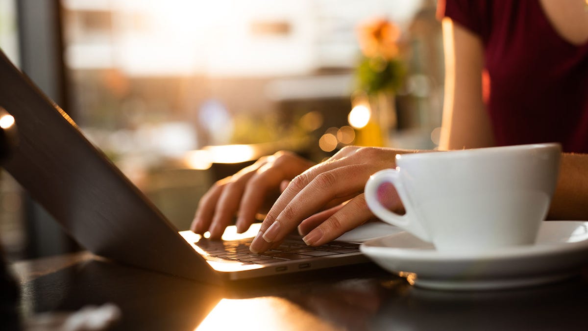 Hand typing on computer with cup