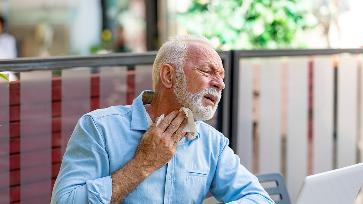 Man wiping at sweat on his neck with a hanky while he sits outside.