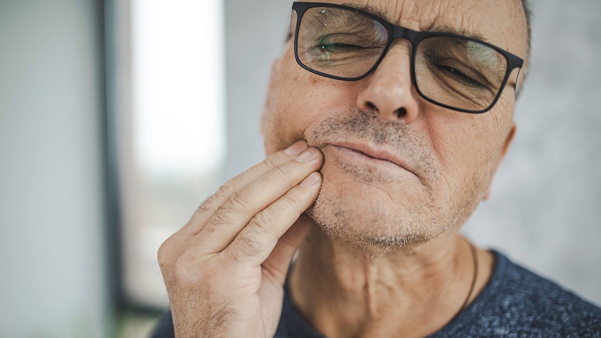 A male carries his cheek in pain, and suffers from dental pain