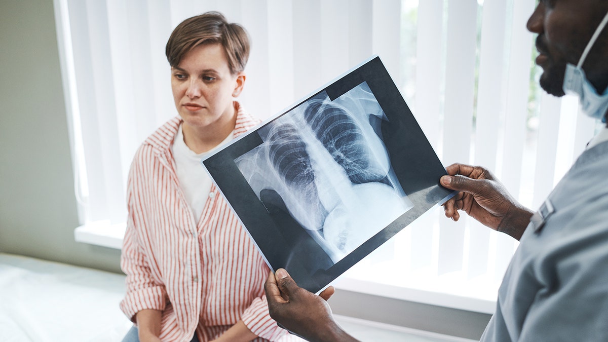 Doctor with x-ray of lungs, standing in front of patient.