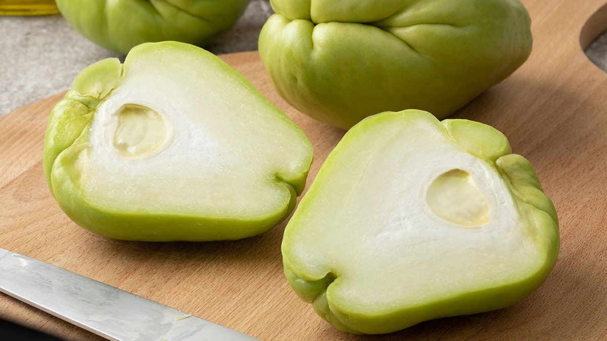 Whole and halved fresh chayote on a cutting board