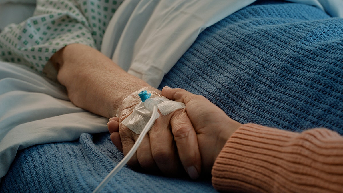 patient holds hands with supporter in hospital bed