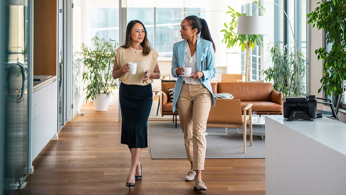 businesswomen converse while walking through an office