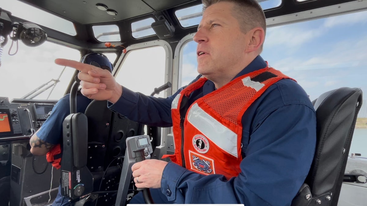 U.S. Coast Guard captain wearing neon orange life jackets pointing at fragments belonging to alleged smugglers along Rio Grande