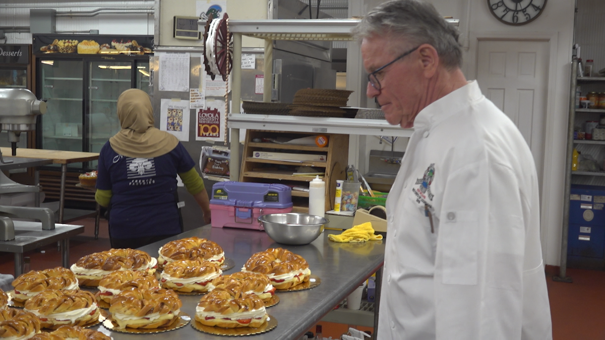 Jean-Luc Albin looks at his King Cake creations inside his bakery. There are several royal cakes sitting on a metal table.