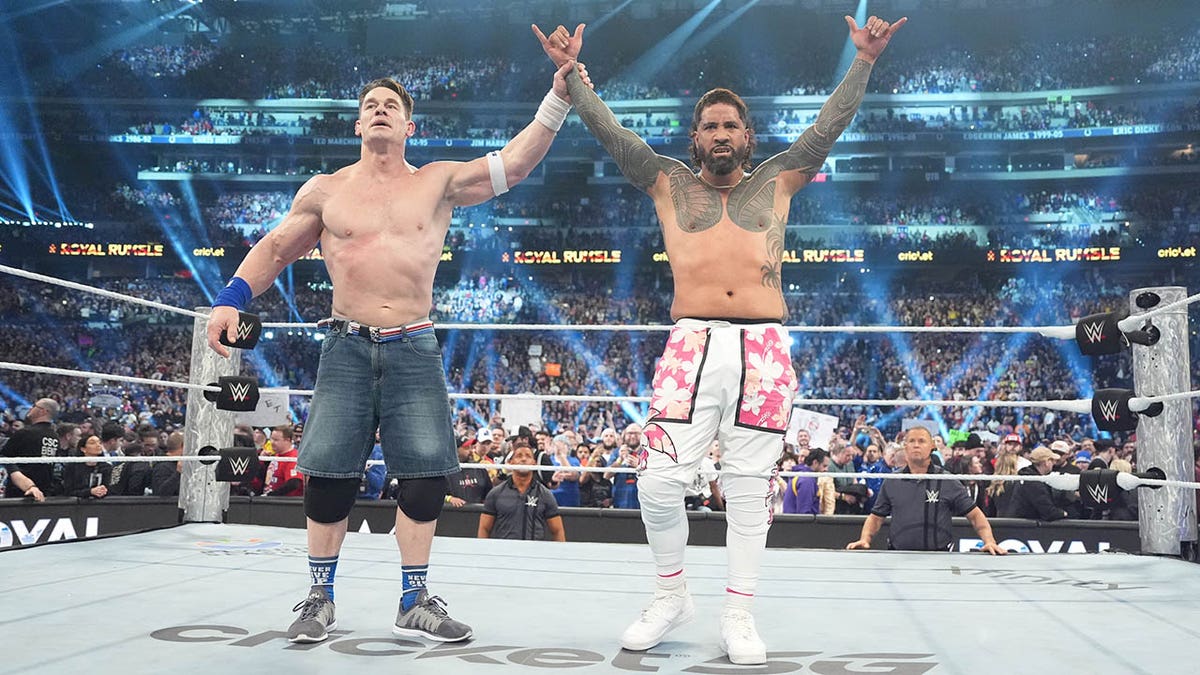 John Cena raises Jey Uso's hand.