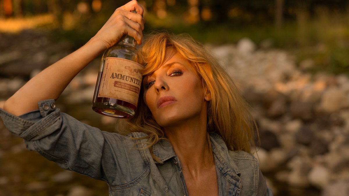 "Yellowstone" histrion   Kelly Reilly presses a vessel  of Ammunition whiskey against her caput  during a photography league   for the California-based whiskey and winemaker.